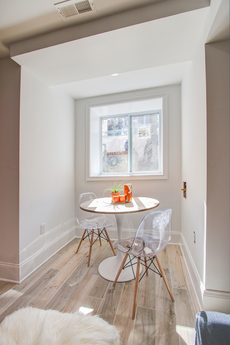 Bright breakfast nook with wood-look tile floors, a white tulip table, two clear chairs, and a window letting in natural light