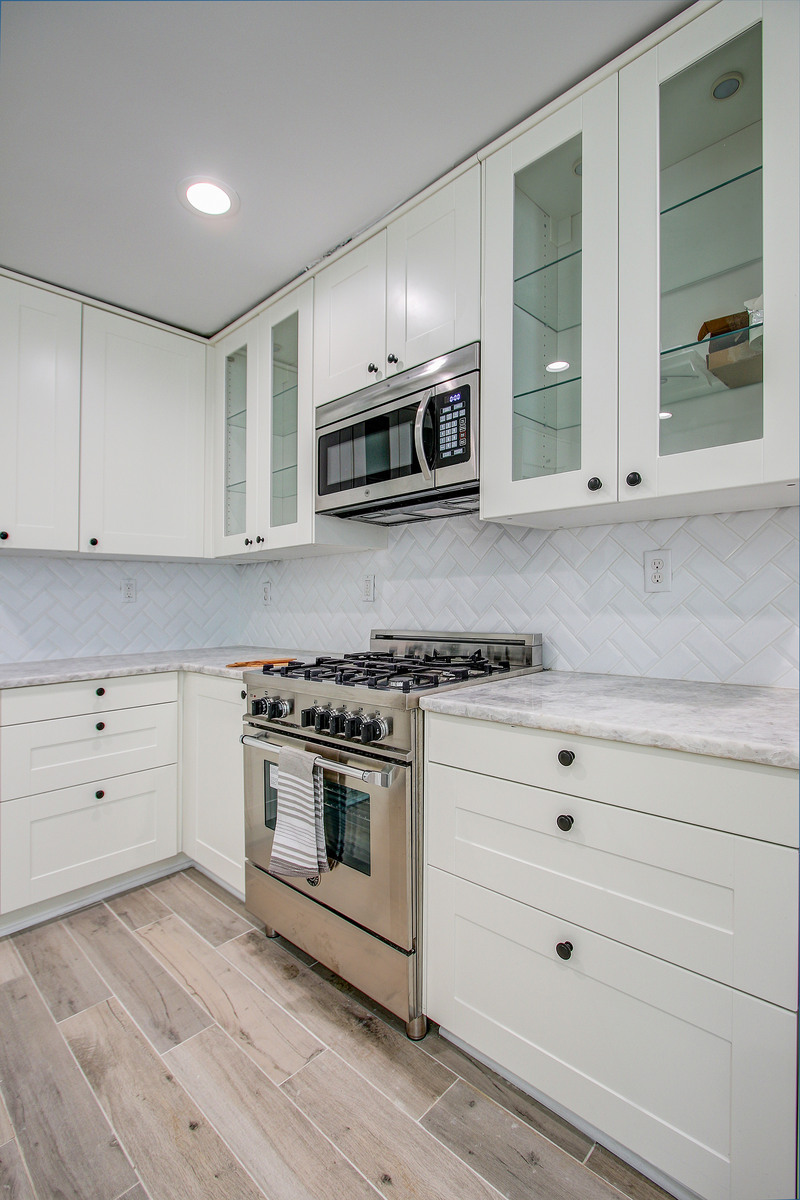 Compact kitchen with white shaker cabinets, glass fronts, a stainless steel gas range, and herringbone tile backsplash Compact kitchen with white shaker cabinets, glass fronts, a stainless steel gas range, and herringbone tile backsplash