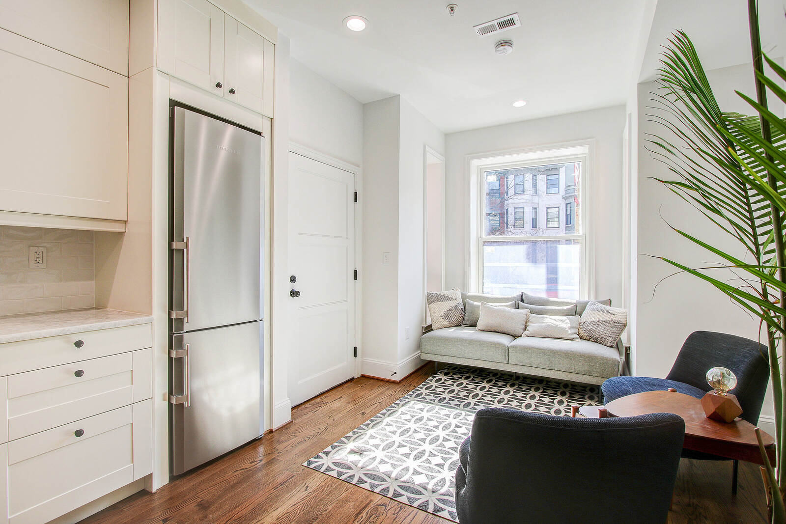 Cozy San Diego sitting area with light-filled window seat, modern chairs, geometric rug, and sleek cabinetry with stainless steel fridge