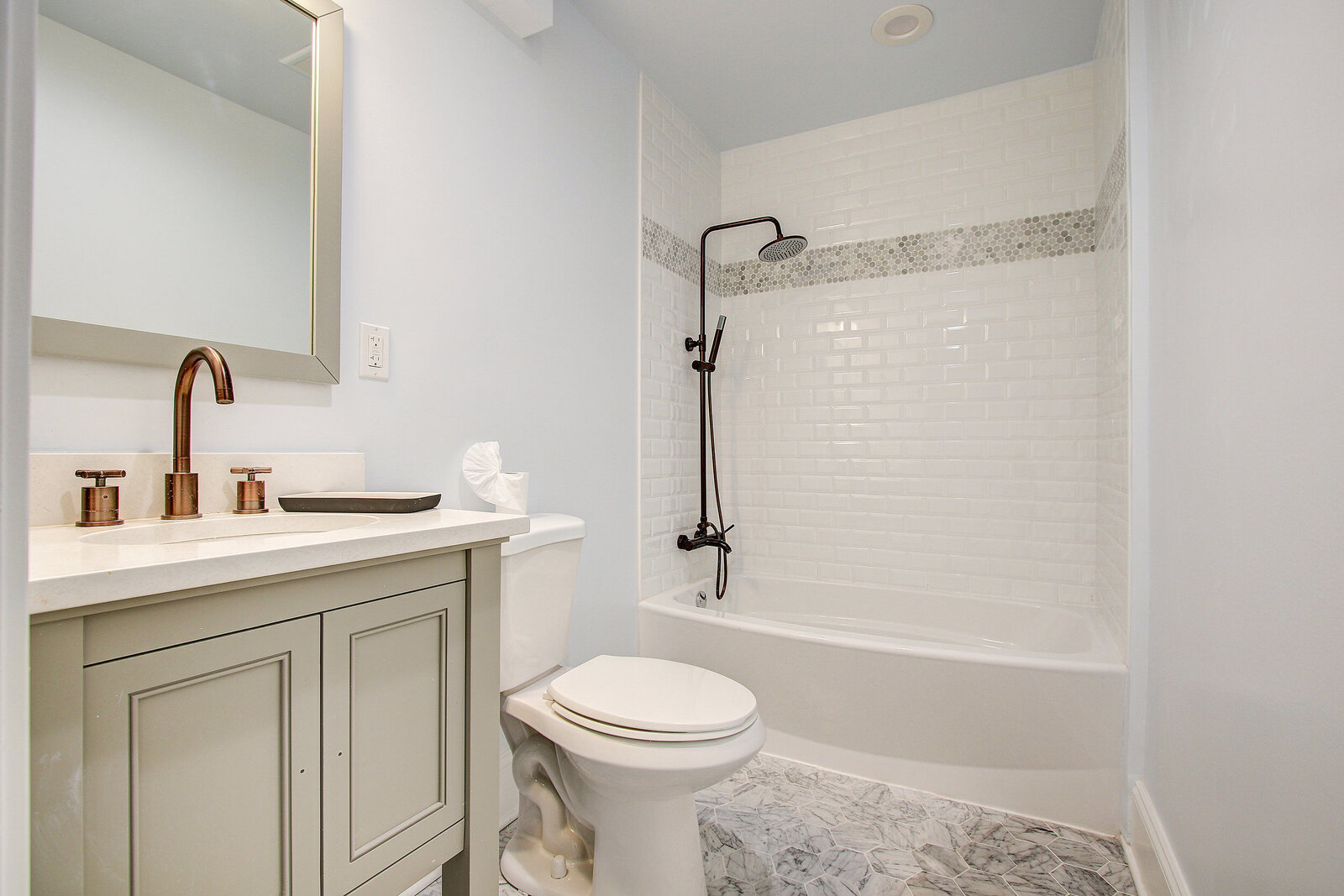 Modern San Diego bathroom with a white vanity, bronze fixtures, subway tile shower, and gray patterned floor tiles
